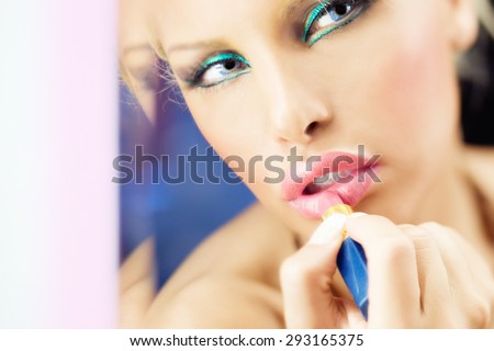 Woman fixing her make-up with lipstick at mirror.