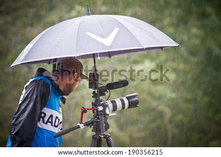 CHAMPERY, SWITZERLAND, SEPTEMBER 21: An unidentified photographer as he stands under an umbrella to protect his gear against the rain during the UCI downhill world championships 2011.