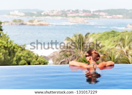 Young woman relaxaing in the swimming pool looking at the ocean view in background