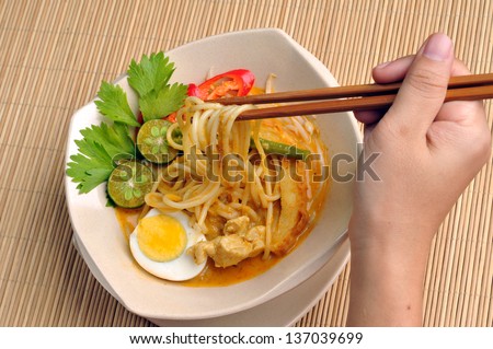 Cropped view of hand holding chopstick to eat curry noodles