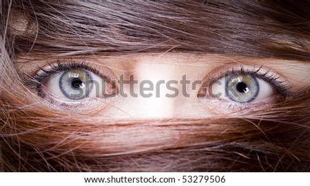 estrange look of a young woman with blue eyes with her hair around the eyes