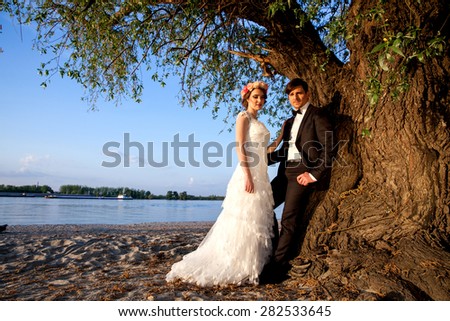 Wedding couple smiling and happy below the tree to the river bank on a beautiful sunny day