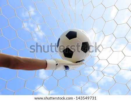 Soccer goalkeeper\'s hands reaching for the ball, with net and sky in the background