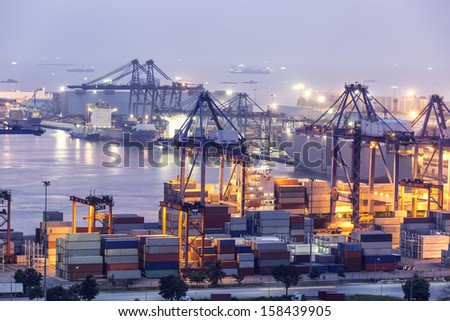 Container Cargo Freight Ship With Working Crane Bridge In Shipyard At Dusk For Logistic Import Export Background