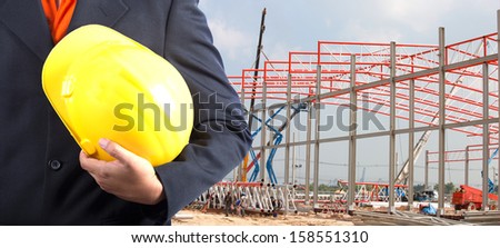 engineer holding yellow helmet for workers security on background of new warehouse buildings and construction cranes on background