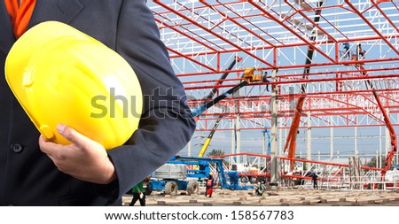 engineer holding yellow helmet for workers security on background of new warehouse buildings and construction cranes on background