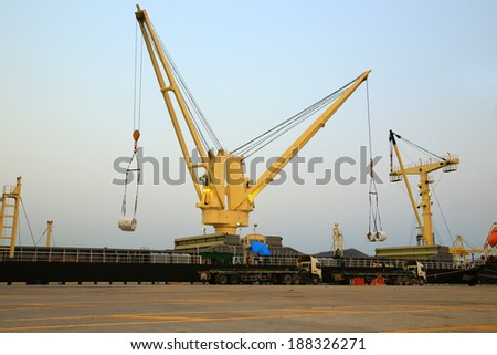 Two yellow cranes at a sea port holding coil steel for transportation by truck at harbor