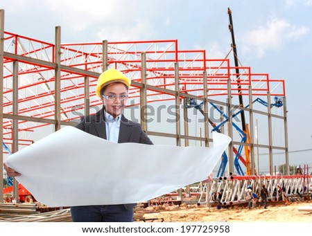 Young female construction specialist reviewing blueprints at construction site background