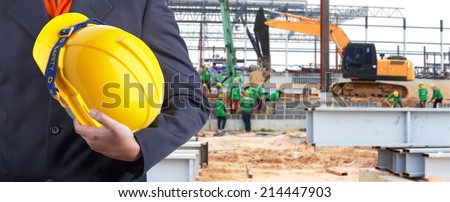 engineer holding yellow helmet for workers security on background of new warehouse buildings and group of worker working hard