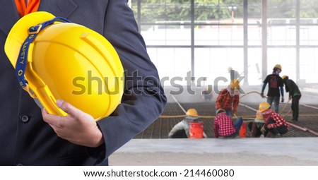engineer holding yellow helmet for workers security on background of new warehouse buildings and worker working hard