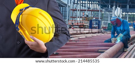 worker or engineer holding in hands yellow helmet for workers security on the background of welding steel for structures roof at workplace