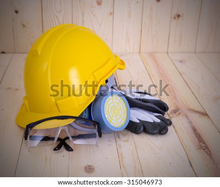 Yellow hard hat with safety equipment on wood background