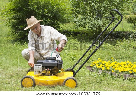 Mid age man oiling and repairing lawn mower in the garden