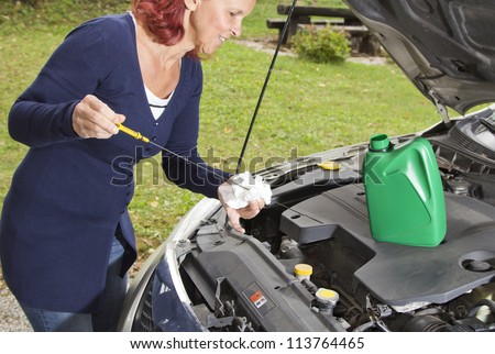 Cute woman driver checking level of oil on a car engine dipstick