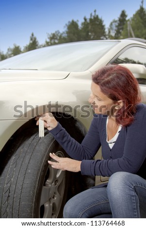 Woman driver measuring tyre profile on car tyre