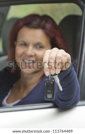 Cute smiling woman driver showing car keys out the car window-selective focus on keys