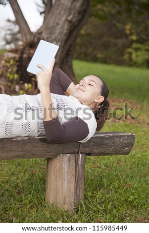 Cute smiling girl with modern tablet PC e-reader, outdoors in the park