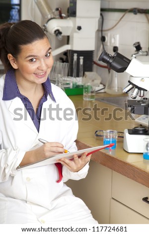 Cute female medical / scientific researcher writing notes whilst using her microscope in a laboratory