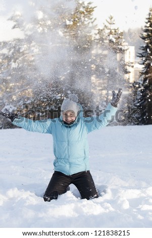 Smiling cute girl outdoors throwing snow in the air on sunny winter day