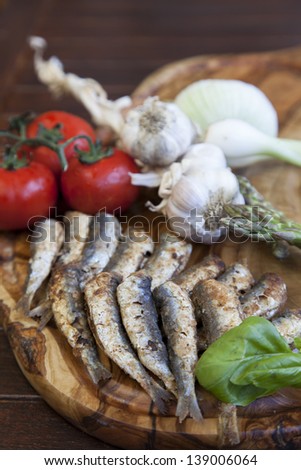 Typical Mediterranean grilled sardines served with fresh organic vegetable, served on olive tree plate, selective focus