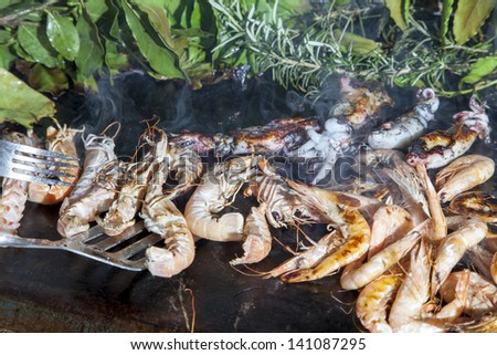Sorting fresh Mediterranean scampi and squids, grilled and smoked with vine leaves, laurel, rosemary and fennel, selective focus
