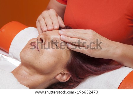 Cute mid aged woman receiving a professional therapeutic facial massage and lymphatic drainage, while lying on a towel in a award-winning health massage center, series of various techniques