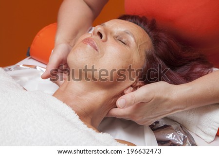 Cute mid aged woman receiving a professional therapeutic facial massage and lymphatic drainage, while lying on a towel in a award-winning health massage center, series of various techniques