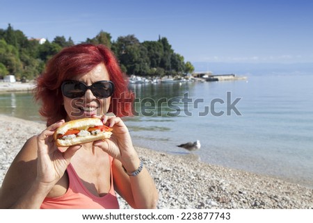 Pretty woman enjoying fresh sea food sandwich on a Mediterranean beach, high resolution photo
