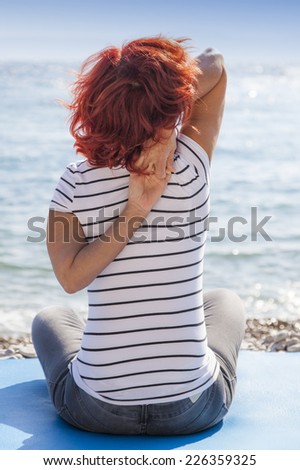 Performing Joga on windy day. Cute woman meditating, performing joga on sea coast, windy sunny day, high, rough sea in the background