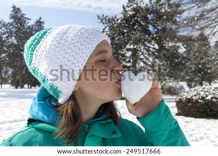 Lovely young woman kissing snow heart , outdoor on a sunny winter day, Love concept. Valentine\'s  Day, selective focus