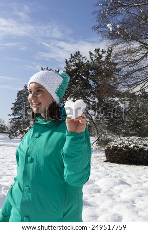 Lovely young woman showing snow heart , outdoor on a sunny winter day, Love concept. Valentine\'s  Day, selective focus