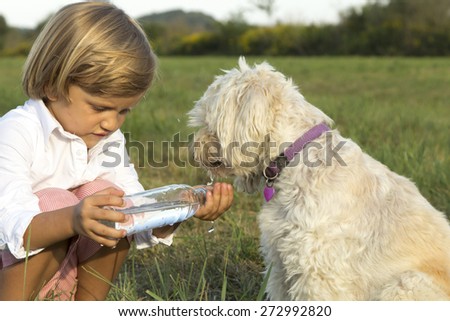 Young cute boy giving water to his dog, whilst playing on the grass