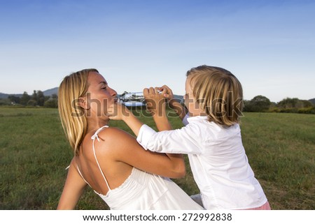 Cute mother drinking water whilst playing with her young son on sunny summer day