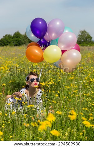Pin up Girl with sunglasses and a lot of colorful balloons on a flowery meadow with dandelions