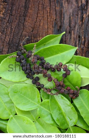 Kaffir lime leaves and dry black peppercorn on wood background