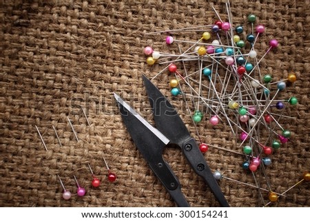Colorful sewing pins with scissors on sackcloth