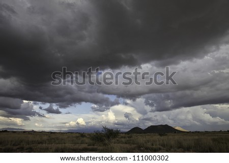 Summer monsoon clouds over low semi-desert grassy landscape/Summer Storm Cloudscape over Low Dry Grassland and Hills/Glimpse of sunlight on a hill during cloudy weather in landscape