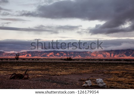 Pink-red color of winter dawn sunlight paints mountains in rural high desert/Dark Pink Sunrise Color on Mountain Range in Winter Semi-Desert Landscape/Winter sunup spotlights desert mountain range