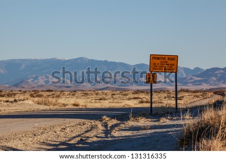PRIMITIVE ROAD caution sign in rural semi-desert United States of America/Sign on Dirt Road cautions to Use At Your Own Risk/Sign says 'PRIMITIVE ROAD...not regularly maintained