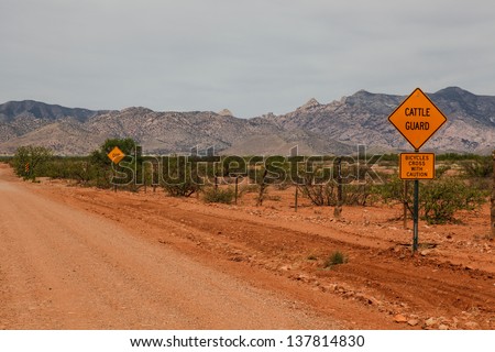 CATTLE GUARD, BICYCLES CROSS WITH CAUTION and DIP road signs along unpaved Old Pearce Road in Arizona state, USA/Road Signs on Desert Dirt Road/Roadside caution signs on dirt road