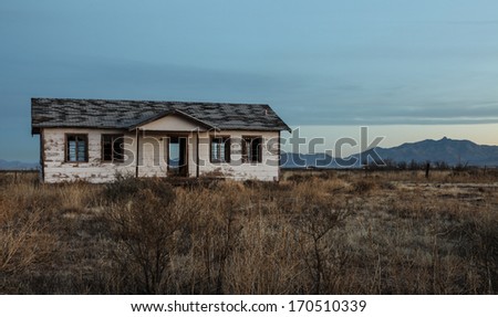 An old, abandoned house built of weather-worn boards and shingle roof stands alone and open amidst semi-desert vegetation/See Through/Old, empty, abandoned house still stands, but now open to weather
