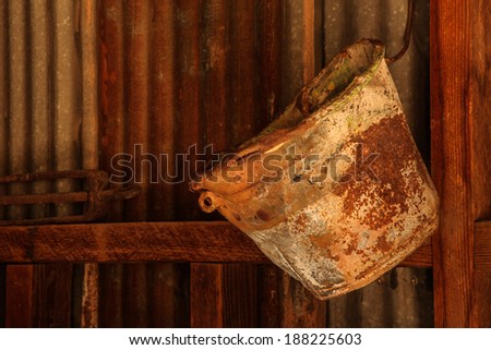 Old rusted bucket hangs against a tin wall inside an abandoned metal shed/Still-Life of Vintage Rusted Bucket hanging on Inside Metal Wall/Rusted pail hangs in vintage metal shed