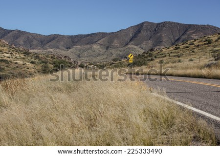Paved road with yellow speed limit sign in dry semi-desert grassland and mountains landscape in Arizona, USA/Dry Grassland and Mountains Landscape with Paved Highway and Sign/Road and sign in dry land