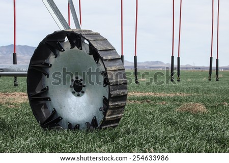 Closeup of wheel of new center-pivot sprinkler system on green crop in southwestern USA/Close View of Wheel of New Pivot Sprinkler System on Farmland in Arizona, United States/Wheel of Watering System