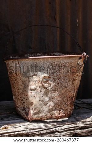 Old U.S. rusty metal bucket in sun and shade/Vintage Battered Rusted Bucket with Fading Letters U.S. in Partial Shade with Sunlight/Weathered rusted battered metal container