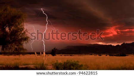 Lightning against dramatic red sunset clouds during desert summer thunderstorm/Desert Grassland with Lightning Thunderstorm and Red Sunset/Lightning and red sunset during monsoon summer thunderstorm
