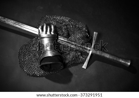 Medieval chain mail, iron gauntlet and a bastard sword still life on a dark background