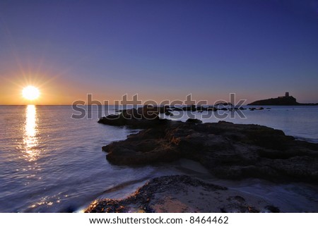 Sunrise in Sardinia with distant lighthouse and stone pier