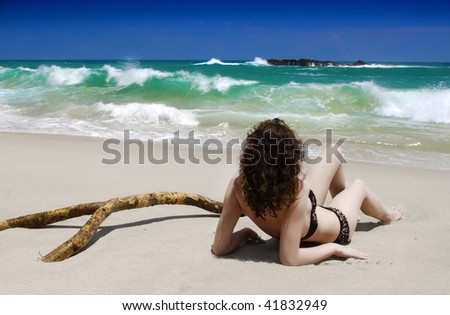 Beautiful young brunette is laying on the beach of the tropical sea with palm branch and watching waves