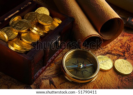 Old brass compass lying on a very old map with treasure chest full of golden coins